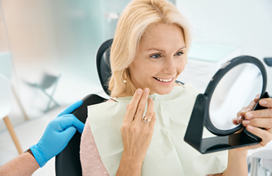 Blonde woman in the dental chair admiring her smile in a mirror