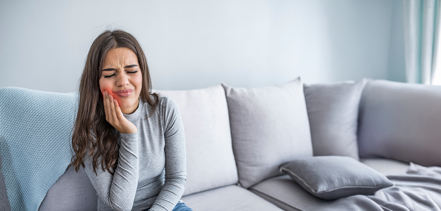 Woman wincing and holding her cheek in pain before seeing an emergency dentist in Grand Prairie