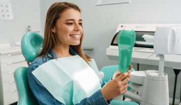 Woman in the dental chair looking at her teeth in a mirror