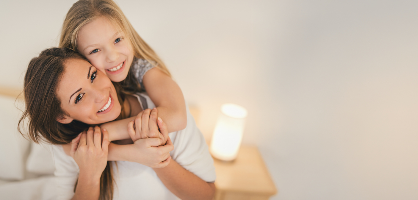 Young girl embracing her mother from behind after a preventive dentistry checkup