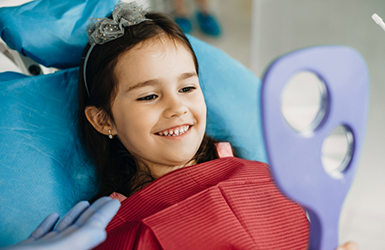 Young girl in the dental chair looking at her teeth in a mirror