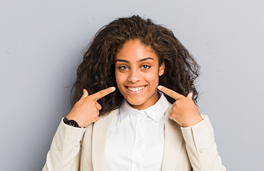 Woman with flawless teeth pointing to her smile