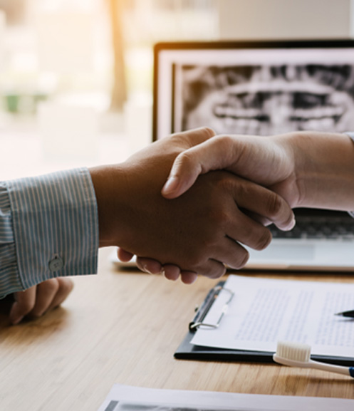 Dental patient shaking dentist’s hand over desk
